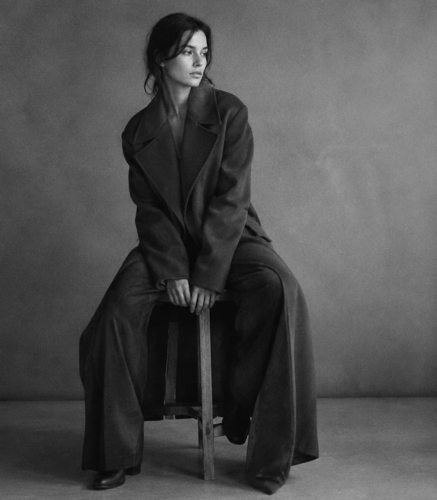 Black and white portrait in an olive coat seated on a stool